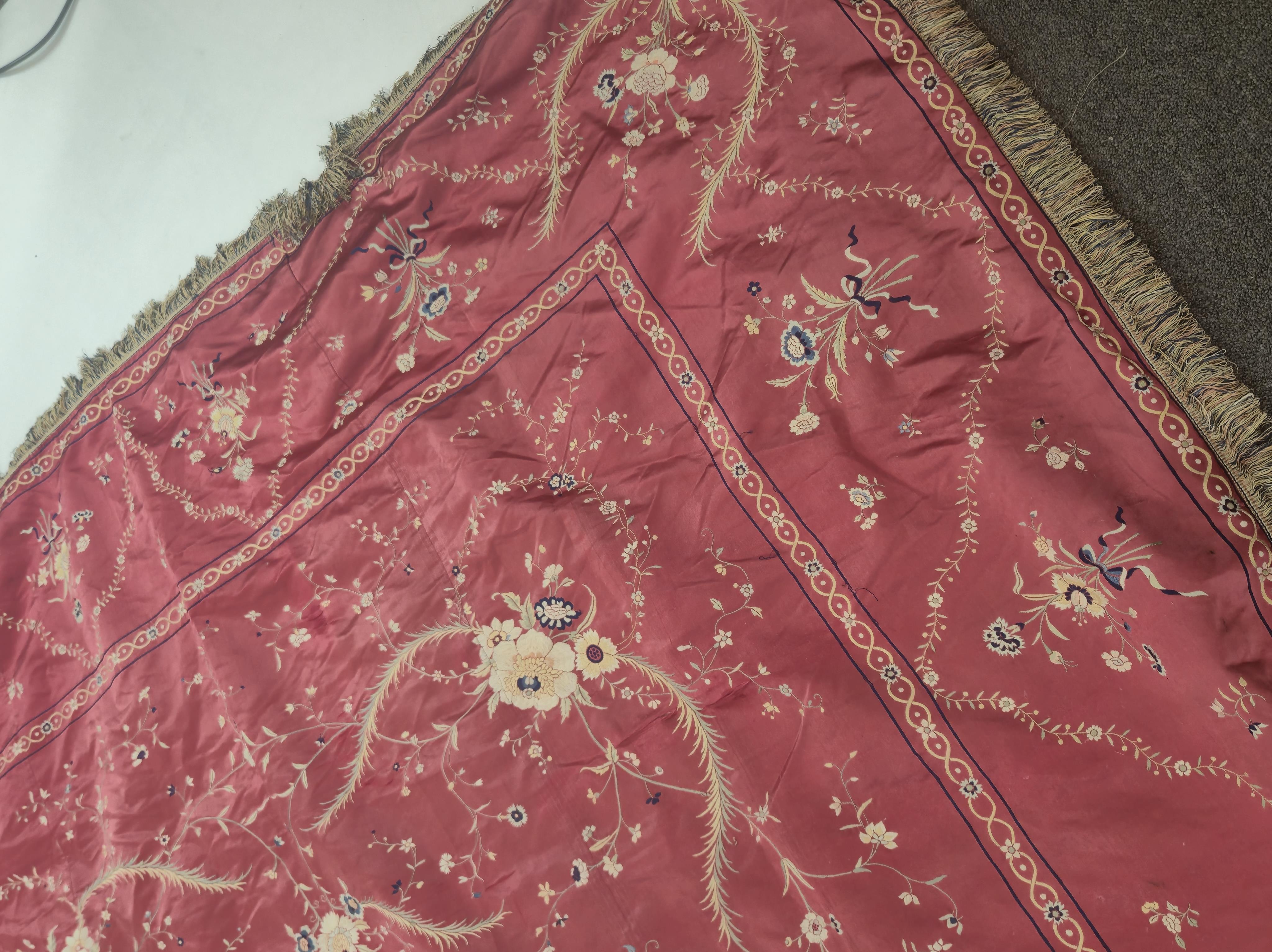 A Chinese 19th century Qing Dynasty crimson red silk embroidered hanging. Embroidered with sprays and swags of flowers and foliage, depicting prosperity and fortune, around a central stylistic sun motif, depicting perfec
